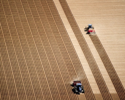 Aerial view of 2 tractors planting potatoes in the fertile farm fields of Idaho, during the spring.