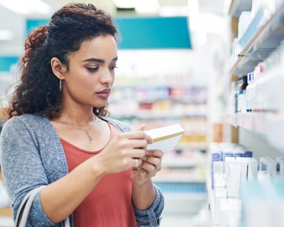 Photograph of a young woman reading the label on a box of medicine in a pharmacy.