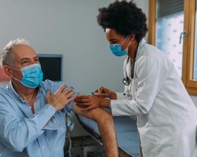 Black female doctor vaccinating elder male