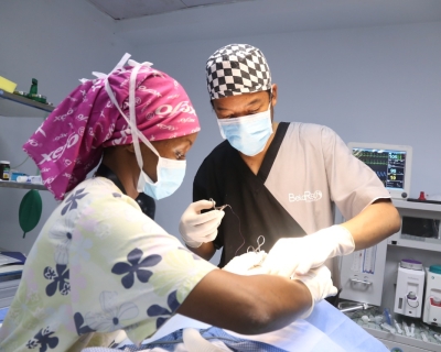 Belinda Karimi, wearing a surgical mask and a hot pink head covering, performs surgery with a colleague.