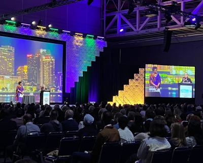 Monique Wasunna stands on a stage delivering her keynote to a packed audience. 